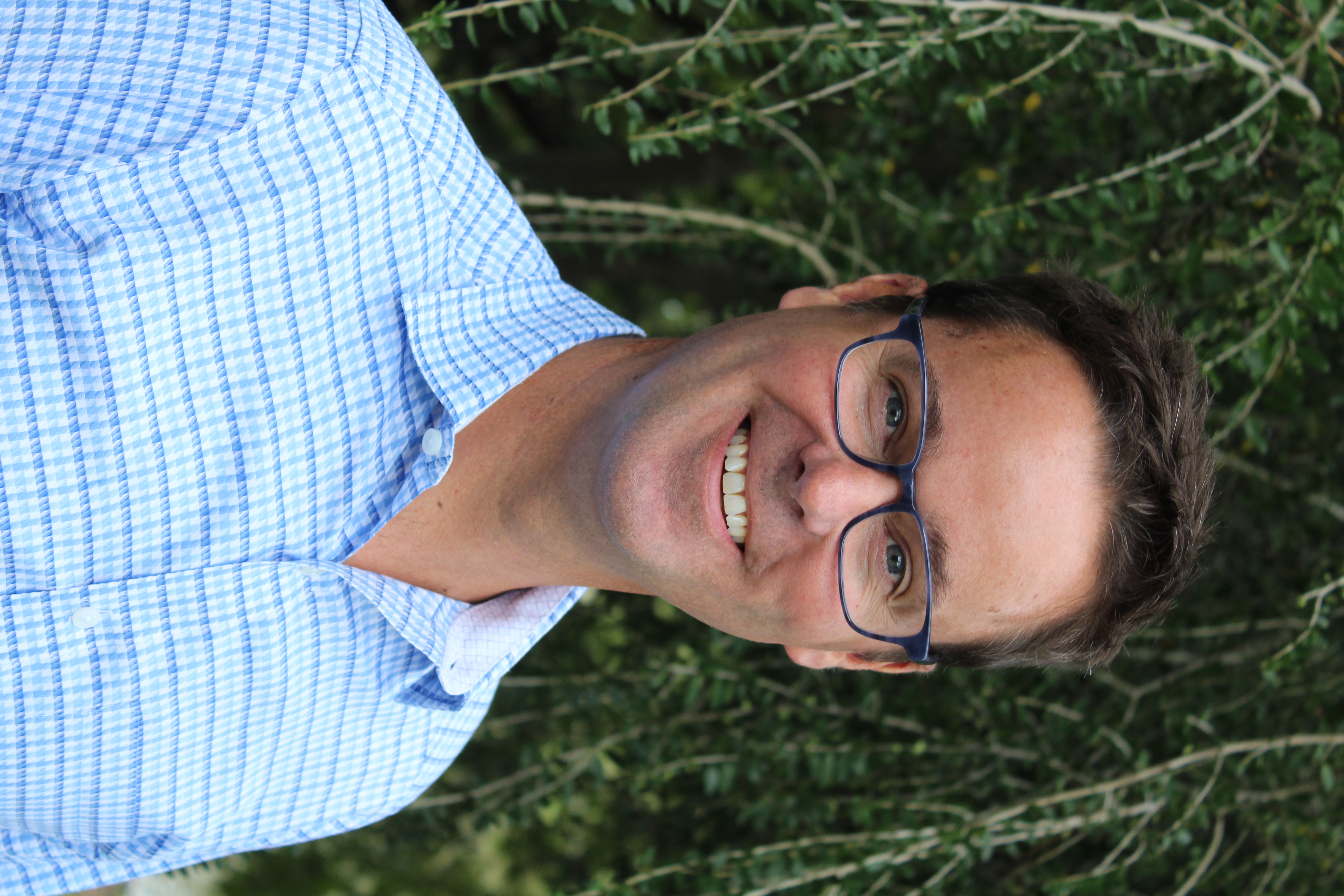 a man with glasses and a blue shirt with short brown hair smiles at the camera